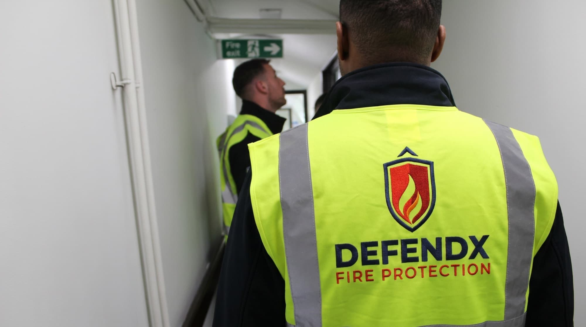 DEFENDX fitters walking a corridor past a fire exit sign